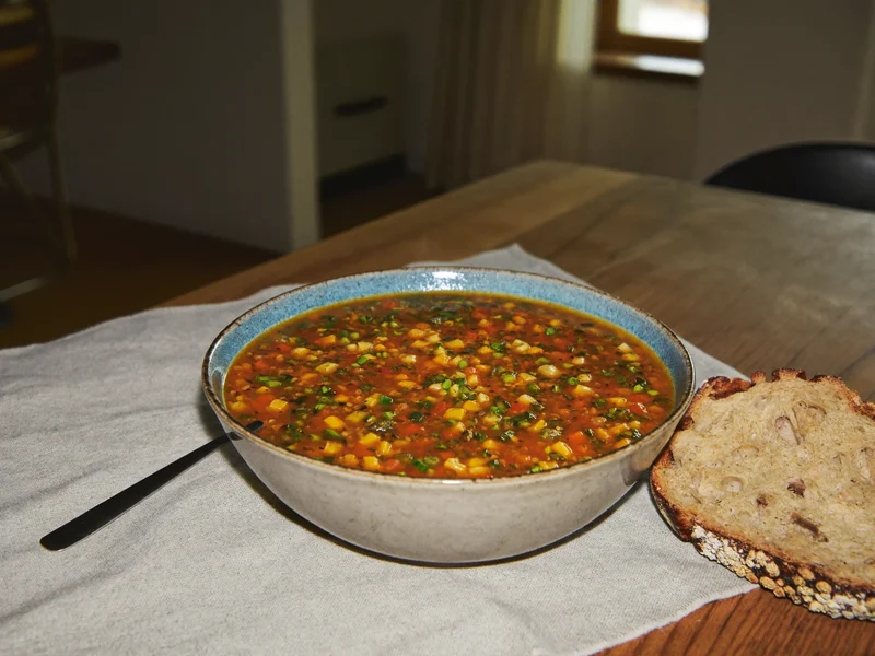 Zuppa fumante di verdure e legumi con pane rustico su tovaglia di lino