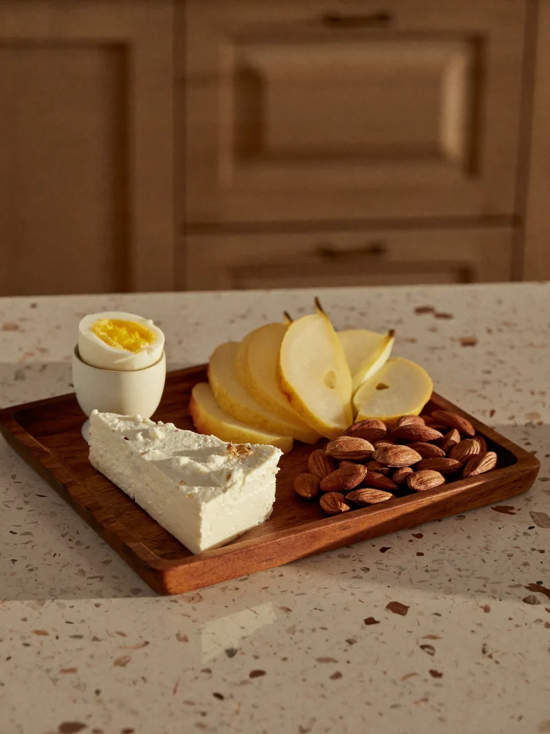 Vassoio di legno con uovo sodo, ricotta, pera a fette e mandorle